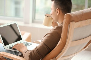 Evde çay içen dizüstü bilgisayarı olan yakışıklı genç adam.