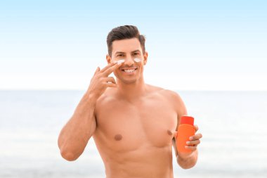 Genç adam deniz sahilinde güneş kremi sürüyor.