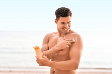 Genç adam deniz sahilinde güneş kremi sürüyor.