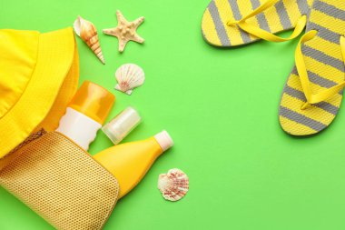 Arka planda güneş kremi, şapka ve parmak arası terlik olan çanta