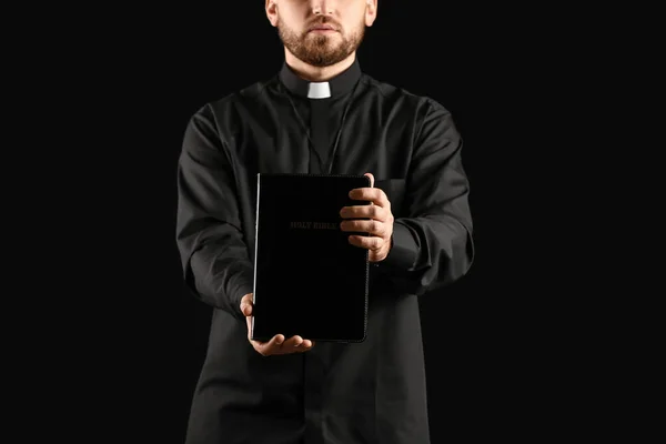 Junger Priester Mit Bibel Auf Dunklem Hintergrund — Stockfoto