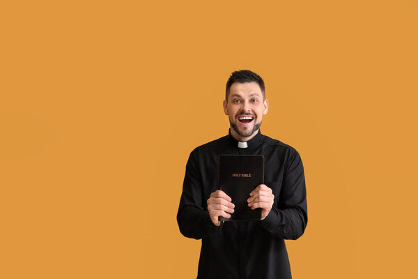 Happy priest with Bible on color background