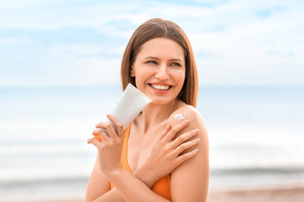 Young woman applying sunscreen cream on sea beach