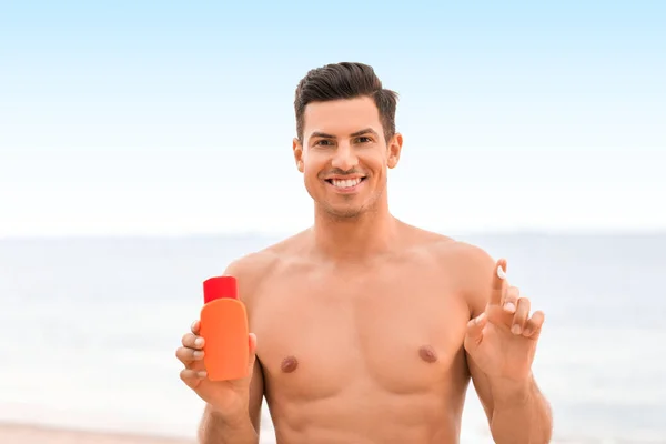 Young man applying sunscreen cream on sea beach