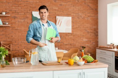 Mutfakta yemek tarifi kitabı olan mutlu bir adam.