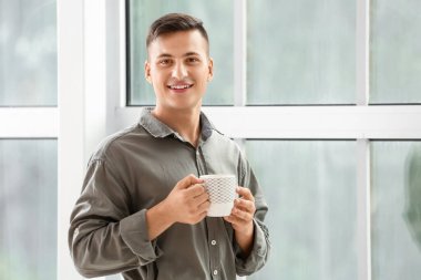 Yakışıklı genç adam evin penceresinin yanında çay içiyor.
