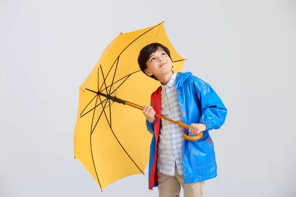 Cute little boy in raincoat and with umbrella on light background