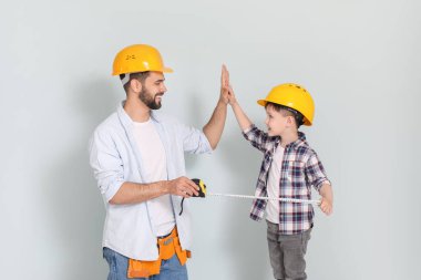 Baba ve oğul ölçü bandıyla gri arka planda birbirlerine beşlik çakıyorlar.