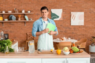 Mutfakta yemek tarifi kitabı olan mutlu bir adam.