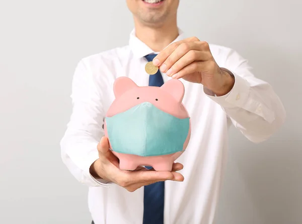 Businessman Putting Money Piggy Bank Medical Protective Mask Light Background — Stock Photo, Image