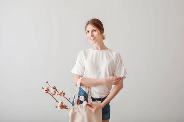 綿の花と光の背景にショッピングバッグを持つ美しい若い女性 — ストック写真