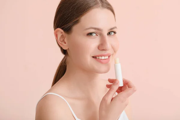 Beautiful young woman with lip balm on color background