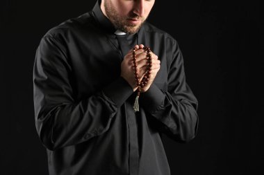 Young priest praying to God on dark background clipart