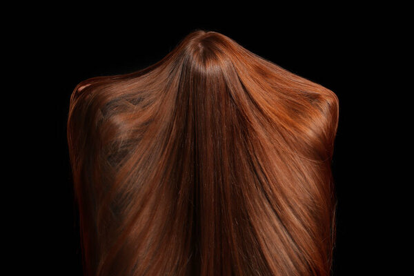 Beautiful young redhead woman on dark background, back view