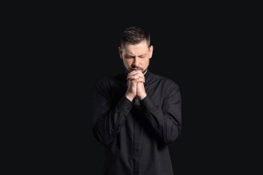 Karanlık arka planda yakışıklı dua eden rahip.