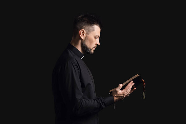 Handsome priest with Bible on dark background