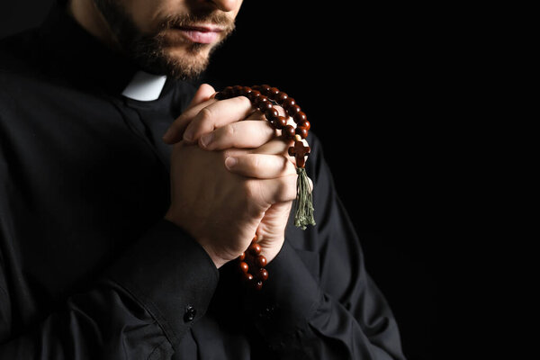 Handsome praying priest on dark background