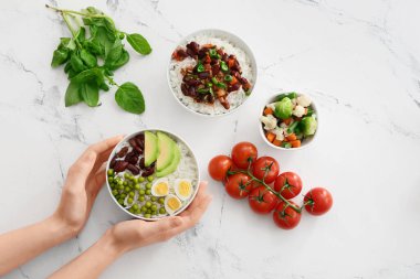 Lezzetli pirinçli kadın elleri ve kasede fasulyeler ve beyaz arka planda sebzeler, üst manzara.