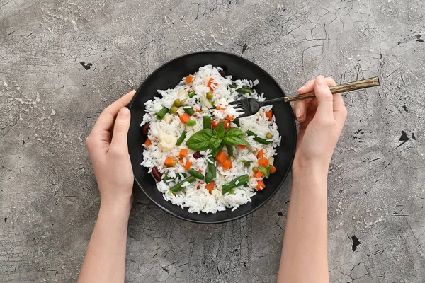 Woman eating tasty rice with beans and vegetables on grey background