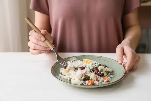 Woman eating tasty rice with beans and vegetables at table