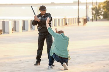 Saldırgan Afro-Amerikan polis memuru dışarıdaki adama kötü davranıyor.