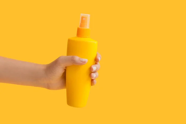 Female hand with bottle of sunscreen cream on color background