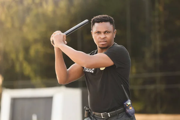 Aggressive African-American police officer with baton outdoors