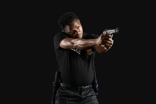 Aggressive African-American police officer with gun on dark background