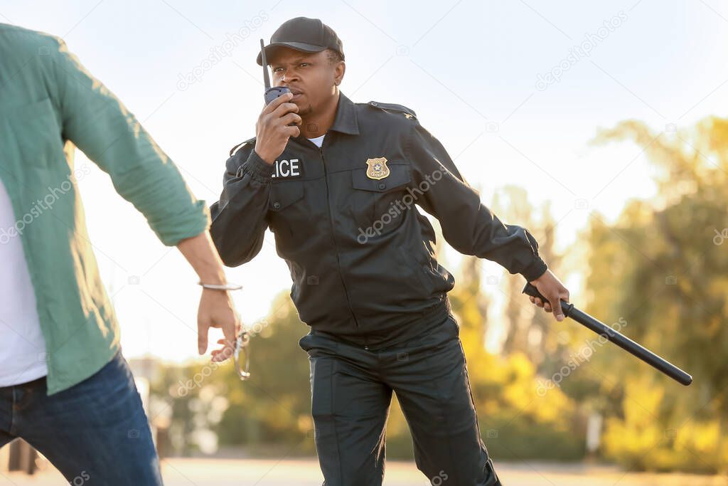 Aggressive African-American police officer mistreating man outdoors