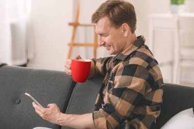 Evde çay içen cep telefonlu yakışıklı bir adam.