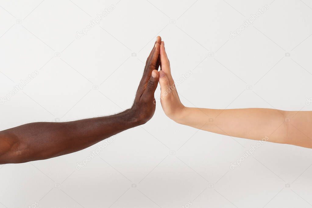 Caucasian woman and African-American man giving high-five to each other on light background. Racism concept