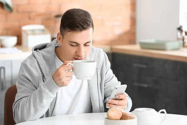 携帯電話のお茶を飲みながら家にいるハンサムな若い男 — ストック写真