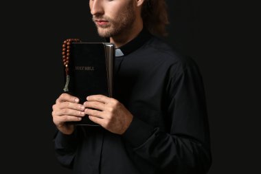 Esmer arka planda İncil 'i olan yakışıklı rahip.