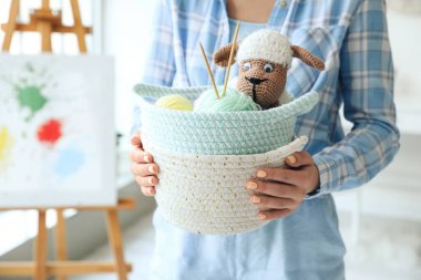 Hasır sepetlerle oyuncak taşıyan ve odada örgü ören bir kadın.