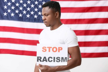 Ulusal bayrağın yanında afişi olan üzgün bir Afro-Amerikalı. Irkçılığı bırak
