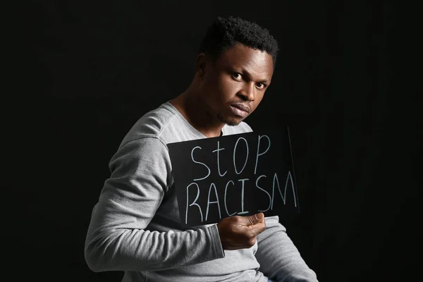 暗い背景にポスターを持つ悲しいアフリカ系アメリカ人の男 人種差別をやめ — ストック写真
