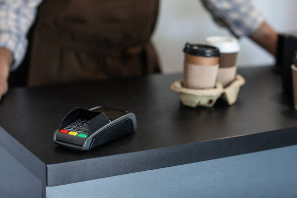 Payment terminal and cups of coffee on counter in cafe