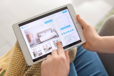 Evindeki otelde tablet bilgisayarlı rezervasyon odası olan kadın.