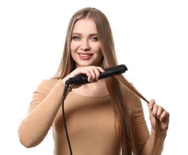 Güzel bir genç kadın beyaz arka planda saç için düz ütü kullanıyor.