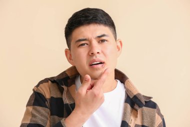 Asyalı bir adam dudaklarına merhem sürüyor. Renk arka planına karşı.