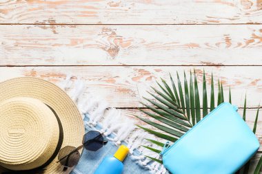 Beyaz ahşap arka planda güneş kremi, güneş gözlüğü ve şapkalı çanta.