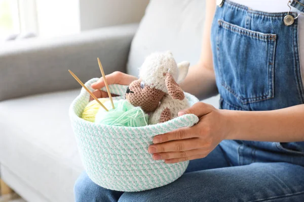 Woman holding wicker basket with toys and knitting yarn in room