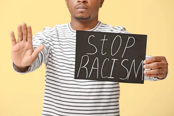 色の背景に停止ジェスチャーを示すポスターを持つ悲しいアフリカ系アメリカ人男性 人種差別をやめ — ストック写真