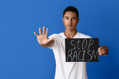 Afro-Amerikalı üzgün genç bir çocuk. Renkli arka planda dur hareketi gösteren bir poster var. Irkçılığı bırak