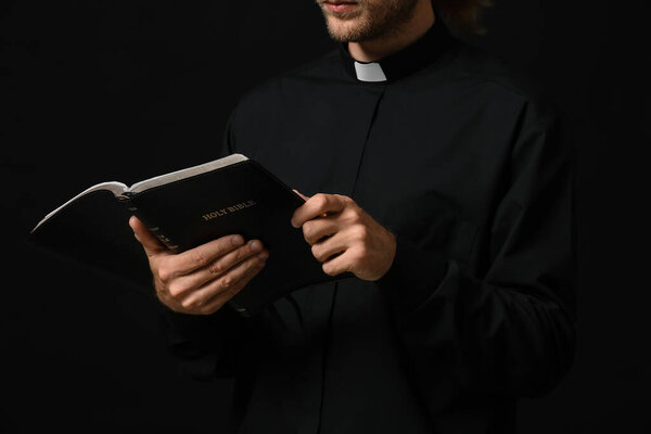 Handsome priest with Bible on dark background