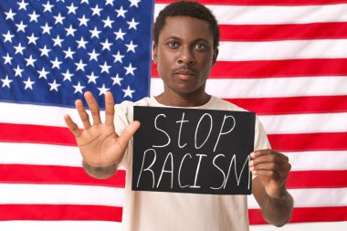 Ulusal bayrağın yanında afiş taşıyan üzgün Afro-Amerikalı bir adam. Irkçılığı bırak