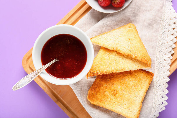 Bowl of tasty strawberry jam and bread on color background