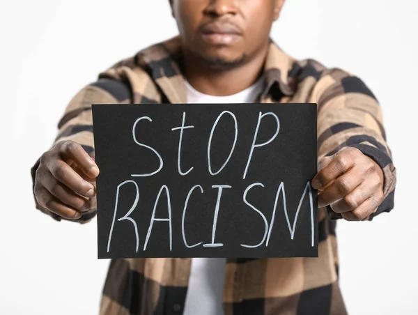 光の背景にポスターを持つ悲しいアフリカ系アメリカ人の男 人種差別をやめ — ストック写真