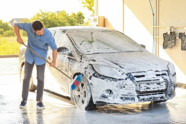 Adam dışarıda arabasını yıkıyor.