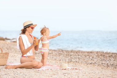 Anne ve küçük kızı sahilde güneş kremi sürüyorlar.